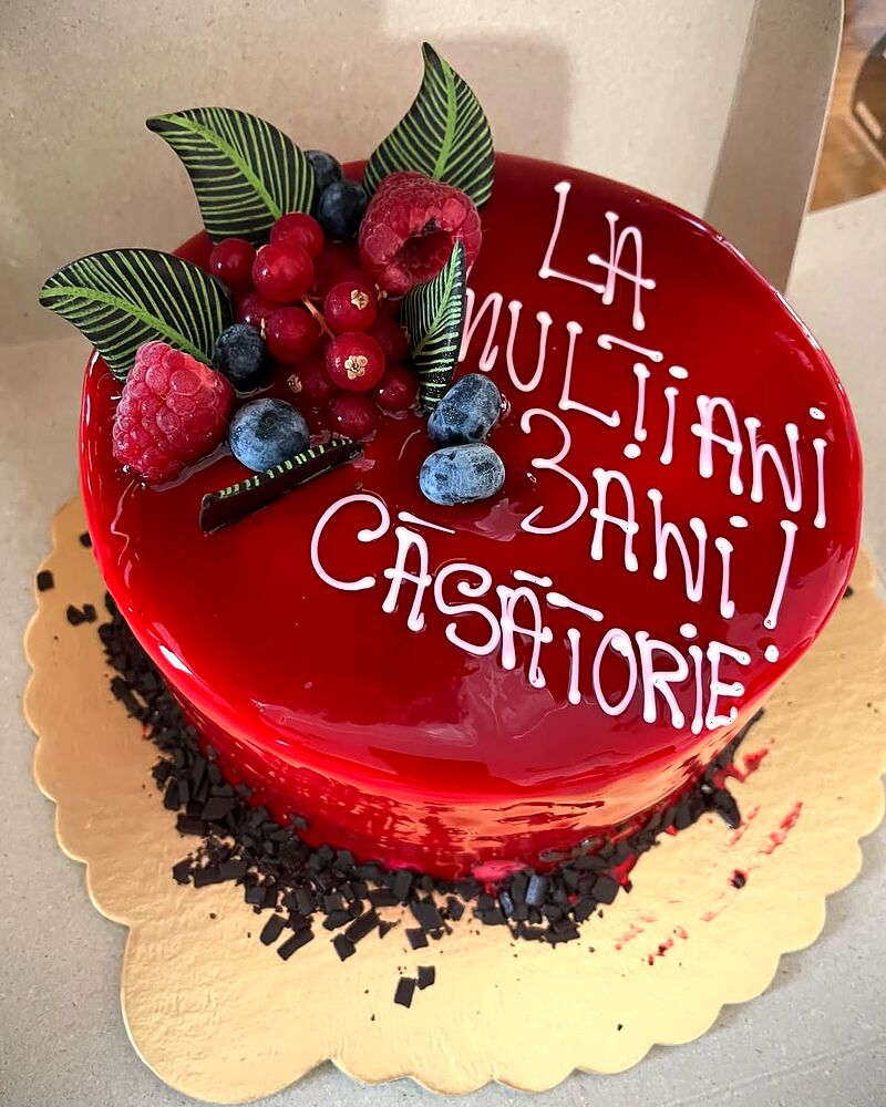Tort cu glazură roșie lucioasă, fructe de pădure și mesaj scris deasupra